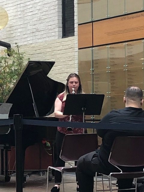 Woman playing clarinet in galleria next to piano
