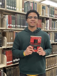 Picture of man standing in front of library bookshelves, holding a book