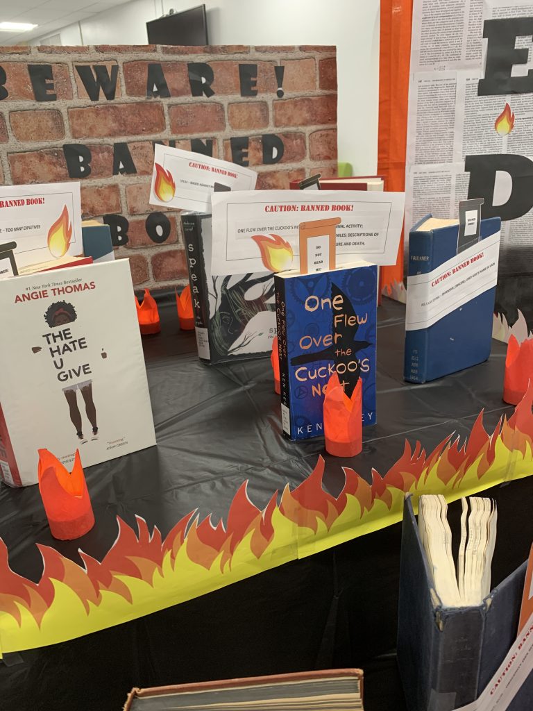 A number of books stand on a black table cloth with small red tea lights in front.