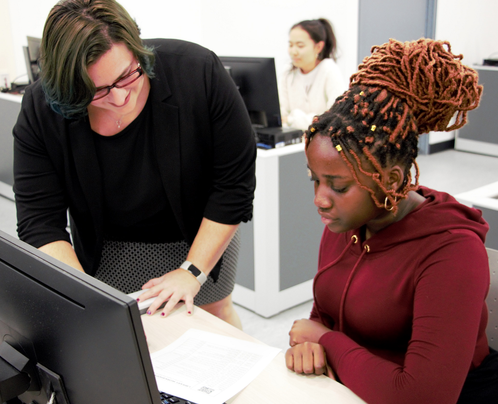 A librarian works with a student at a computer station. 