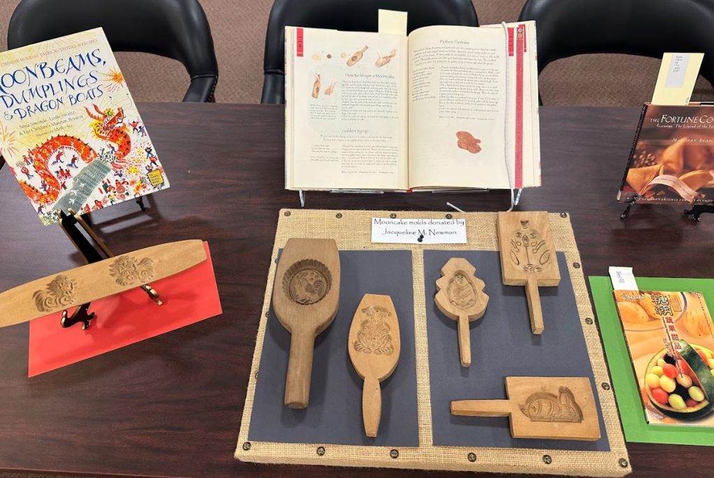 Photograph of four books about Chinese desserts and six mooncake molds. Taken at the Art Crawl in Special Collections. Melville Library, Stony Brook University on April 26, 2023.