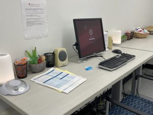 Picture of a desk with desktop computer, plants, white noise machine, and soft lighting.