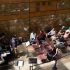 AI: Group of people sit in chairs watching pianist play, brick wall and glass windows behind (AI-generated alt-text)