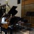 AI: Man with dreadlocks plays light brown guitar on chair outside brick music store; black music stands, backpack on nearby chair (AI-generated alt-text)