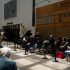 AI: Outdoor University of St. Thomas event in Minneapolis with sign, sculpture, stage, performers, crowd on folding chairs, person behind railing (AI-generated alt-text)