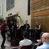 AI: Four musicians indoors: two standing violinists left, two seated cellists, brick wall with painting, window visible (AI-generated alt-text)