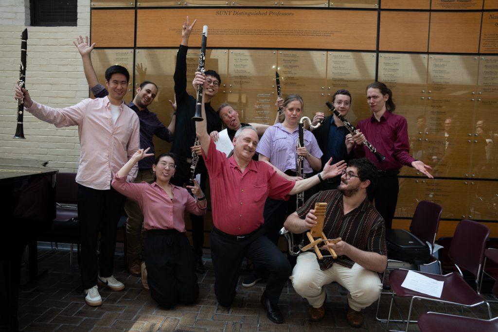 AI: Jazz band indoors, pink and black outfits, brass instruments, brick wall, banner, window with posters, lively camaraderie (AI-generated alt-text)