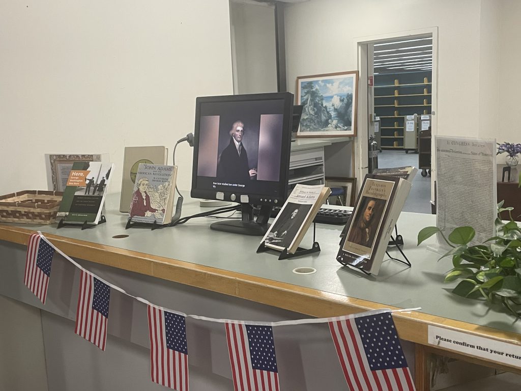 Picture of circulation desk counter decorated with American flag banner and displaying books and computer monitor.