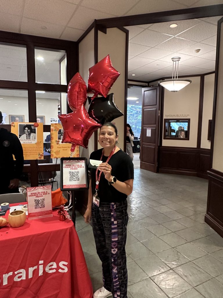 AI: woman in shirt and purple rabies pants holds red balloon at table with sign rabies and other balloons, office background (AI-generated alt-text)