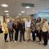 AI: Group in library under Library Services sign; diverse clothing: black jacket, yellow top, blue shirt, white blouse, red top, beige top (AI-generated alt-text)