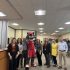 AI: Mascot in red and white Cardinals uniform holding 'Go Cardinals' sign, surrounded by coworkers near a desk with a monitor (AI-generated alt-text)