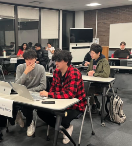 Shows pairs of students working together at desks with laptops out.
