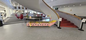 Interior of a library with a central curved staircase, colorful cardboard boat, and red seating areas.