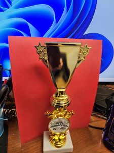 ​Gold trophy with star motifs in front of a red backdrop and a blue patterned screen.