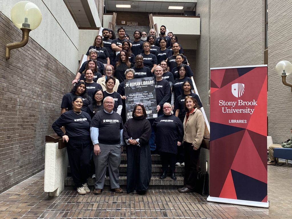 Diverse group of people standing on a flight of stairs next to a Stony Brook University Libraries sign.